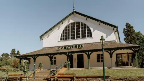 Steven Gallagher The front of Strathpeffer Pavilion on a sunny day with clear blue skies. The words "SPA Pavilion" can be seen in gold lettering on the front of the building.