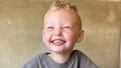 Family photograph The late three-year-old Albie Speakman who has blond hair and a beaming smile wearing a grey t-shirt 