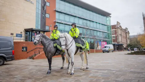 West Midlands Police Two female police officers in uniform sit on horses outside a University of Wolverhampton building.