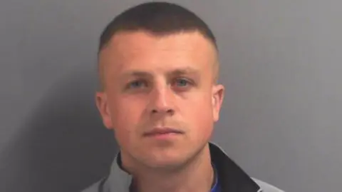 Mugshot of Euan Corbett. He is clean shaven with short dark hair shaved at the sides