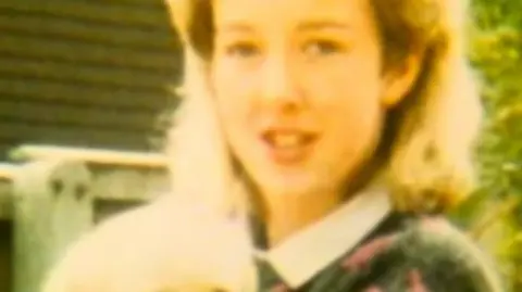 Diane Sindall, who has blonde hair, smiles at the camera while holding a light coloured puppy which appears to be a labrador