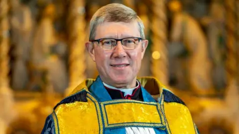 Ely Cathedral Mark Bonney with short fair hair and glasses wearing yellow vestments