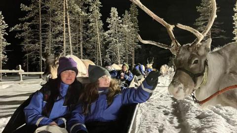 Mum and daughter sit in a sleigh as Lily-Rae reaches out to touch the reindeer