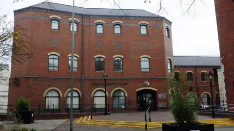 Exterior shot of Grimsby Crown Court. It is a red-bricked building with parts of it set over several floors. It has arched windows and steps with yellow lines leading to the entrance.