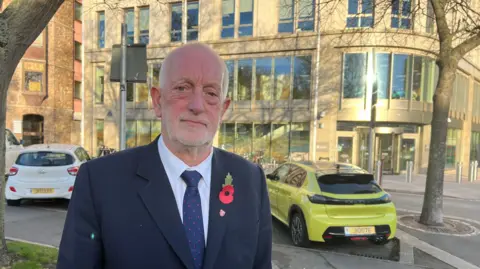 Jersey's Minister for the Environment, Deputy Steve Luce, outside the Government of Jersey offices in Union Street in St Helier, wearing a navy blazer, shirt and tie.