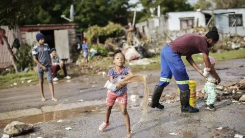  Gianluigi Guercia/AFP  A child helps clearing water from an area damaged by floods in Uitenhage on June 05, 2024. Flooding caused by torrential rain and fierce winds on South Africa's eastern coast have killed at least 22 people, local authorities said on Tuesday. Flooding hit several locations in two eastern provinces, two rare tornados were spotted, temperatures plunged and snow fell in some central regions.
