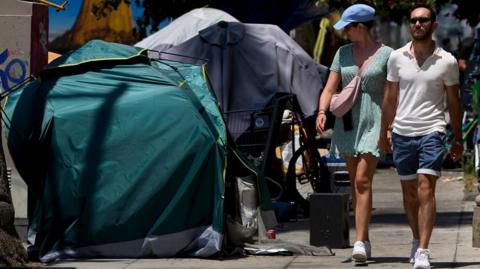 A man and woman walk past a tent on a sidewalk in Los Angeles