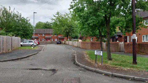 BBC A photo of Abram Close with red brick houses on the right and brown wooden fencing on the left