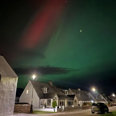Allison MacLean Red and green aurora in the sky above houses in Ullapool.