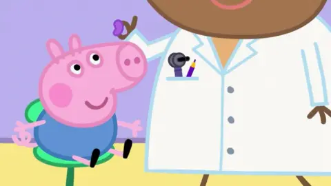 Milkshake/PA Wire Animation of George pig receiving a hearing aid from an audiologist. George is a small little pink pig and he is sitting in a green chair. He is looking up and smiling at the audiologist, who is wearing a white coat, passes him a small blue hearing aid.