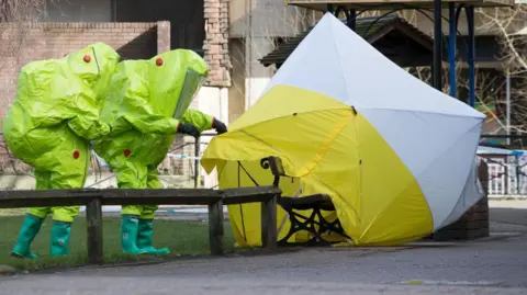 Getty Images Specialist officers in lime green protective suits secure a police forensic tent covering the bench where Sergei and Yulia Skripal were found on 4 March 2018