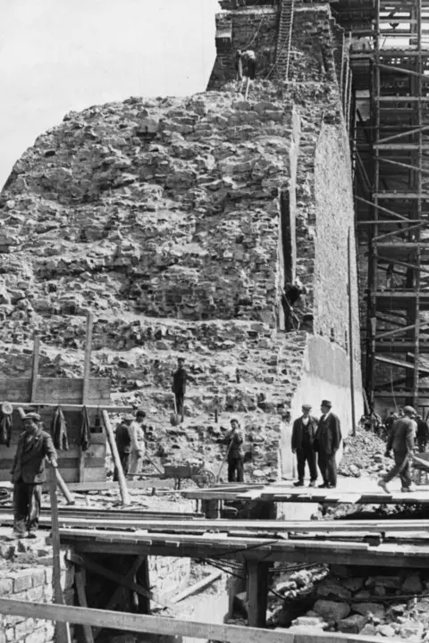 The Möhnesee Archive Men stand on construction platforms and carry planks of wooden scaffolding at the site of the damaged dam.