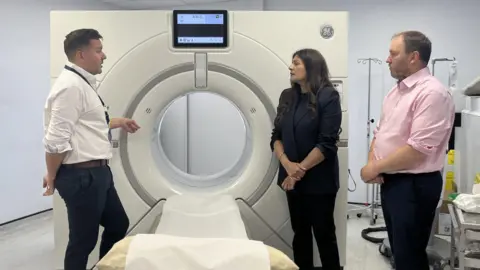Two men and a woman standing near a CT scanner.