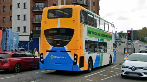 A bus in Peterborough - driving on the road with cars on either side of it.