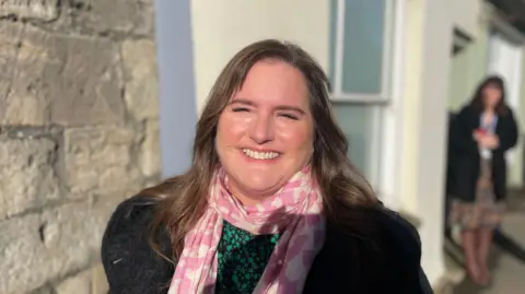 Alison Figueiredo smiling at the camera. She has brown hair and is wearing a pink scarf with a black jacket.