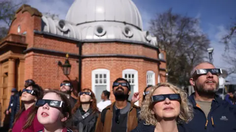 EPA-EFE/REX/Shutterstock/ Neil Hall People wearing protective glasses observe a partial eclipse from the Greenwich Observatory in 2025