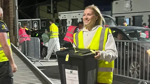 Ballot papers being brought in at Plymouth count - a female volunteer carries a ballot box 