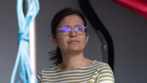 National Oceanography Centre Dr Tillys Petit is wearing a green and white striped t-shirt. She has on glasses and is looking off camera to something in the distance.