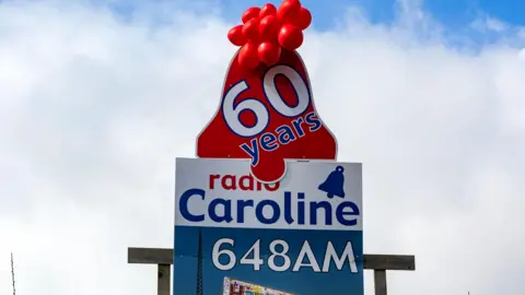 Radio Caroline billboard celebrating the station's 60th birthday in 2024, it is blue and white with red balloons at the top.