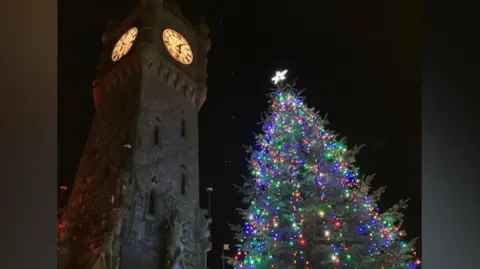 A lit up Christmas tree next to a church