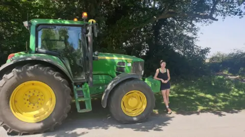 Wenham Grange Georgina Langton McColl wearing a black playsuit and standing next to a green tractor