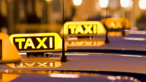 Getty Images Taxis lined up in a row at night with neon yellow TAXI signs visible