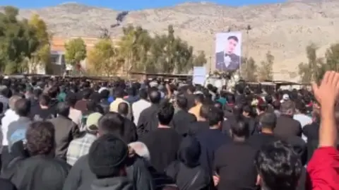 X Crowd at a commemoration with one person on the right raising his hand