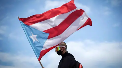 Getty Images Puerto Rican reggaeton singer Bad Bunny waves a Puerto Rican flag as he takes part of a demonstration demanding Governor Ricardo Rossello's resignation in San Juan, Puerto Rico on July 17, 2019.