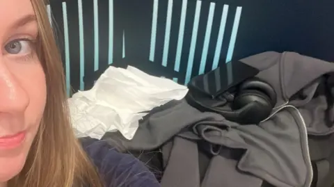 Kiera sitting in the airport, with a makeshift bed of bags and jackets behind her