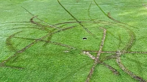 Crosby Bubble / LDRS Trails of damage can be seen on the green around a hole at the golf course, with the grass torn up and soil visible beneath.