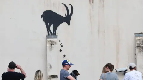 Reuters La gente mira una cabra pintada con spray en un lado de una pared.