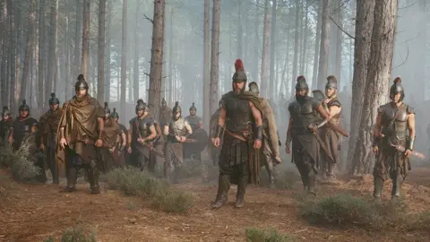 Matt Damon, centre, as Odysseus, stands with a group of men in Greek armour and helmets in Culbin Forest.