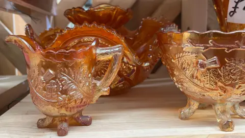 Pieces of patterned vintage orange glassware sit on a wooden shelf