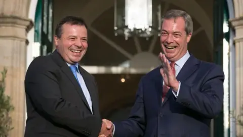 Getty Images Arron Banks and Nigel Farage, pictured in 2014 in bright sunshine, shaking hands and smiling broadly.
