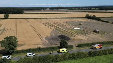 YappApp  aerial image of plane crash in a field, a fire engine and air ambulance are in the field. On the road a number of emergency vehicles are in attendance. 