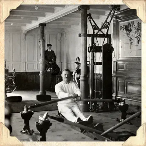 Una fotografía en blanco y negro de un hombre usando una máquina de ejercicios en un gimnasio en el Titanic (foto de Getty Images)