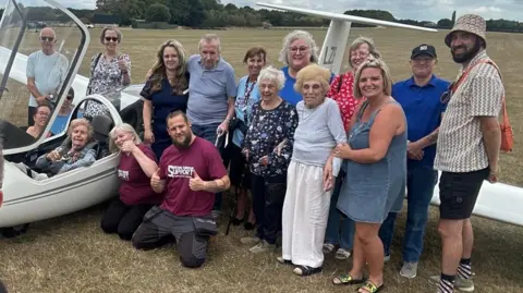 Rob Barsby Mrs Gilliver sits in the cockpit, with friends, family and carers standing next to the plane 