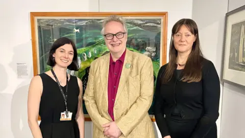Swindon Borough Council Three people stood in front of a painting which features rocks.