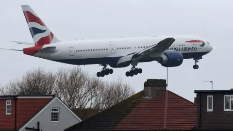A British Airways passenger plane flies near houses as it makes its landing approach to Heathrow Airport