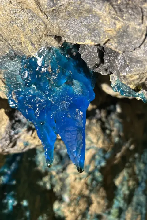 Lucy Dusgate A translucent crystal hangs from the roof of the tunnel. The light shining on it reveals its mid-blue colouration.