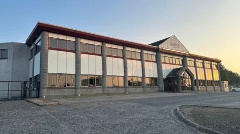 The frontage of the Scotbeef abattoir building in Inverurie, Aberdeenshire - an industrial building with lots of glass windows and an area of tarmac for cars in front