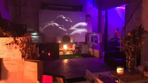 Lucy Blackledge Inside a cosy room with candles and a projector screen showing a black and white film.