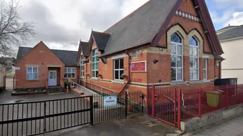 Google Maps An older, Victorian-style red brick school building with short metal fences around it.