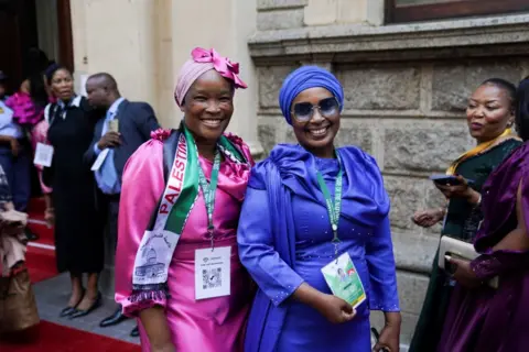 Tamu Nic Bothma / Reuters, mengenakan gaun merah muda dan biru, tiba di negara bagian itu berbicara dengan karpet merah dan berpose untuk foto di luar Balai Kota di Cape Town, Afrika Selatan.