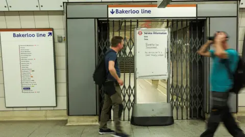 Reuters Passengers walking through Waterloo Underground station and a sign saying the Bakerloo line was suspended