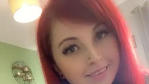 Georgina James Georgina James has red long hair and is smiling at the camera