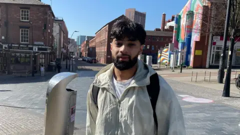BBC/Tom McDougall A young Asian man with a beard stands in a light jacket in a city centre 