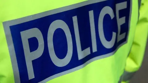 The back of a fluorescent coloured police jacket. The word "police" is written in silver on a blue background. 