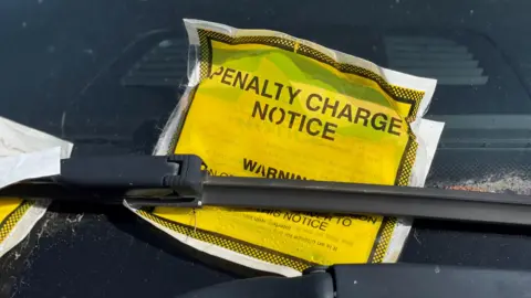 A close-up photo of a yellow parking fine stuck underneath the windscreen wiper of a car.