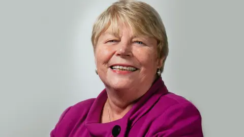 Baroness Jenny Randerson smiles at the camera. She is wearing a purple top.